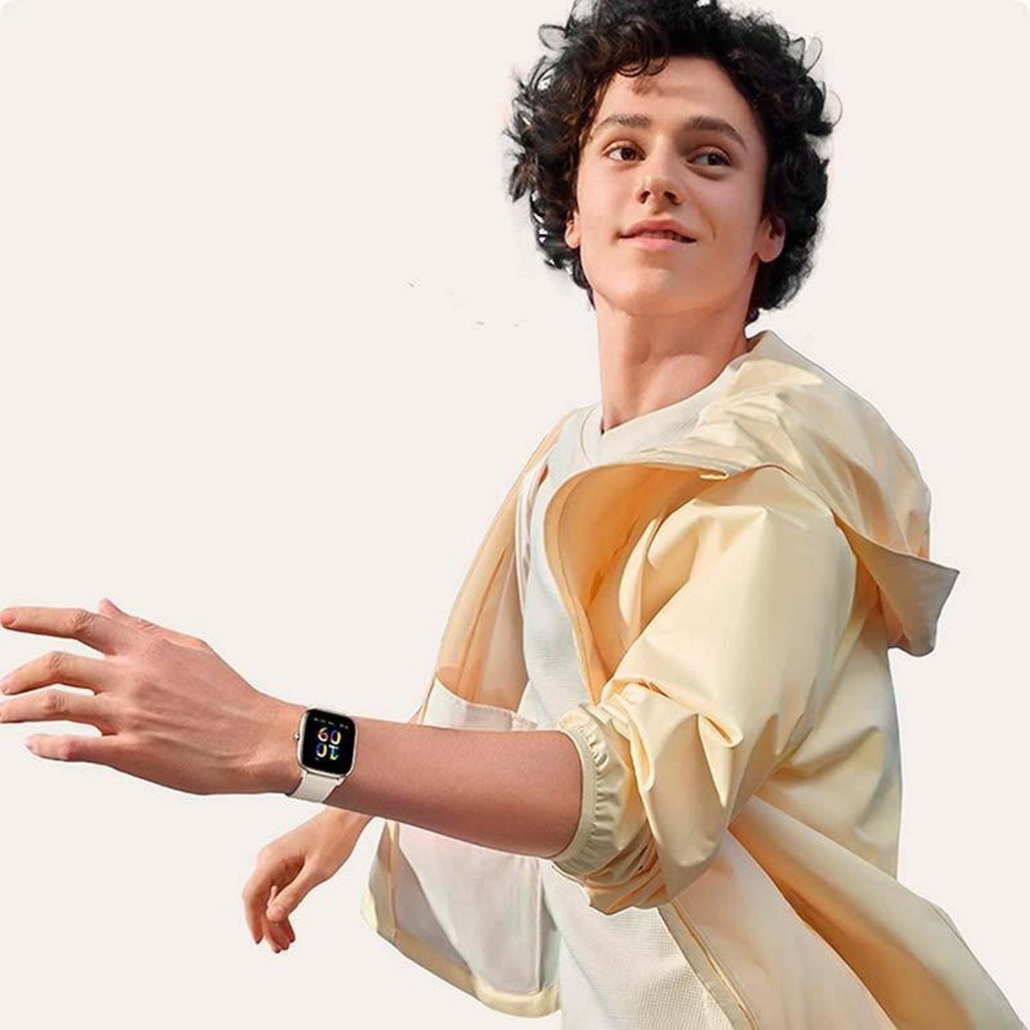 Joven con chaqueta amarilla que lleva un reloj inteligente blanco. Señala con el brazo y la mano derechos.