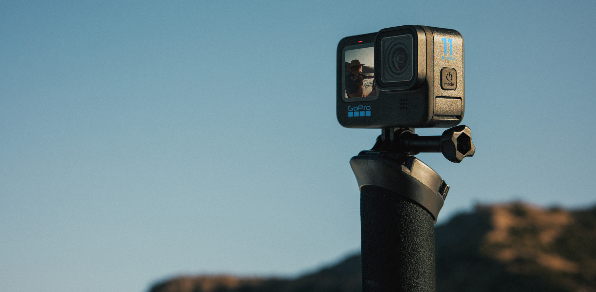 Eine schwarze GoPro-Kamera an einem Griff, blauer Himmel im Hintergrund.