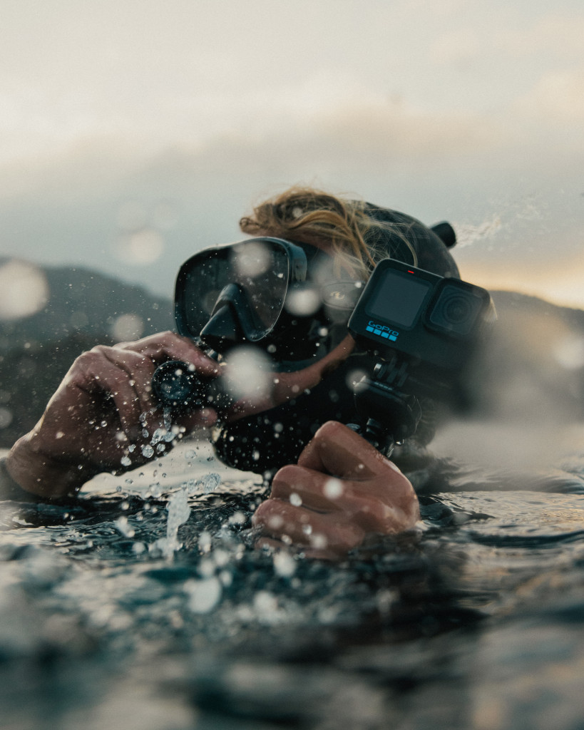 Person im Wasser mit Tauchmaske und GoPro, Wasser spritzt.