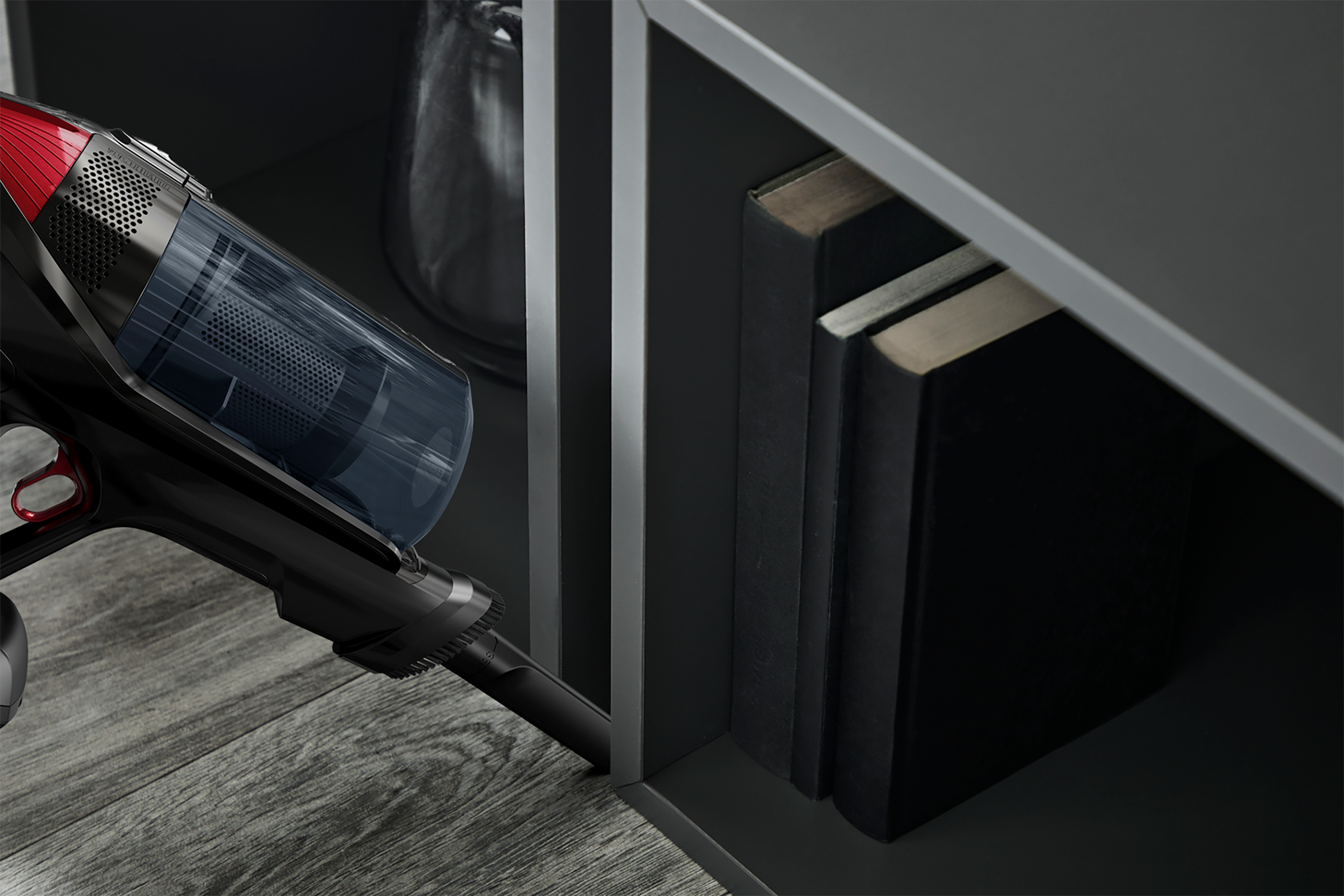 A black and red cordless vacuum cleaner cleans a dark cabinet.