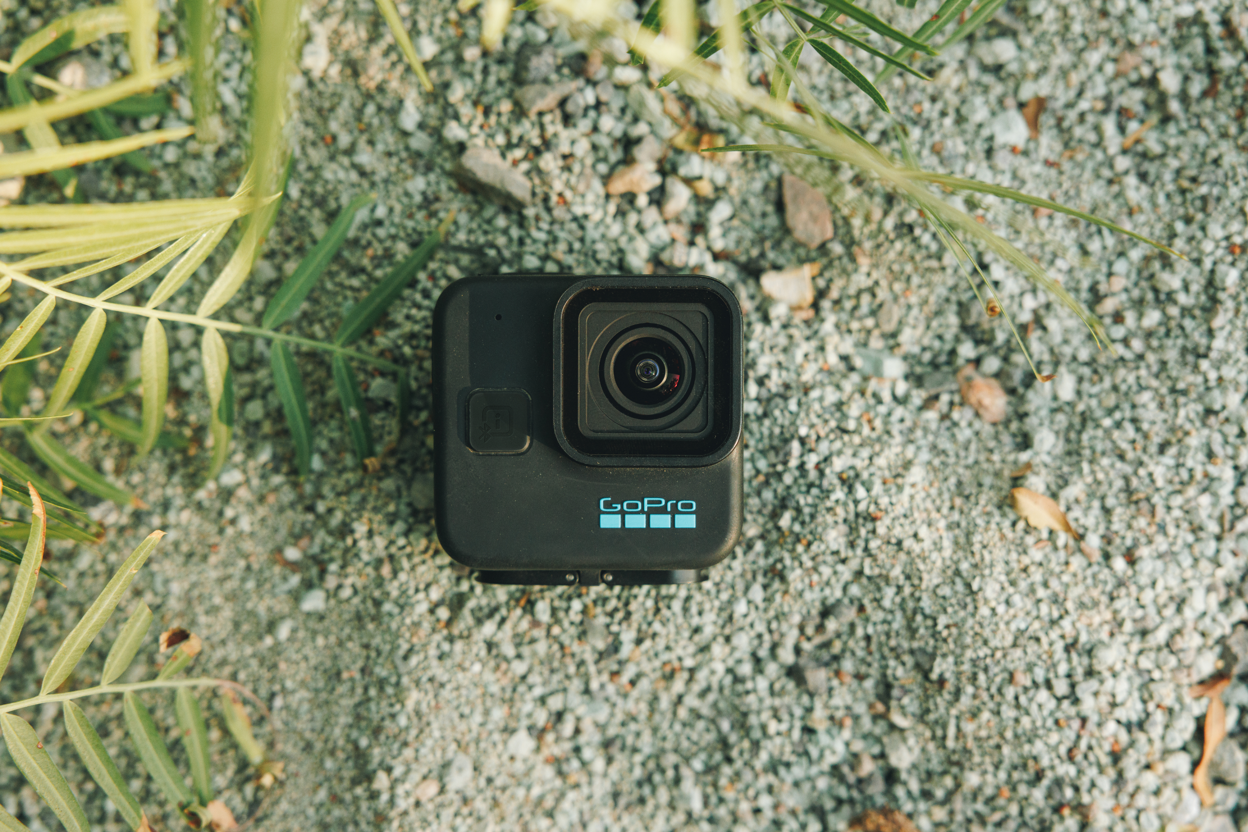 Schwarze GoPro-Kamera liegt auf einer Oberfläche aus kleinen grauen Steinen und grünen Pflanzen.
