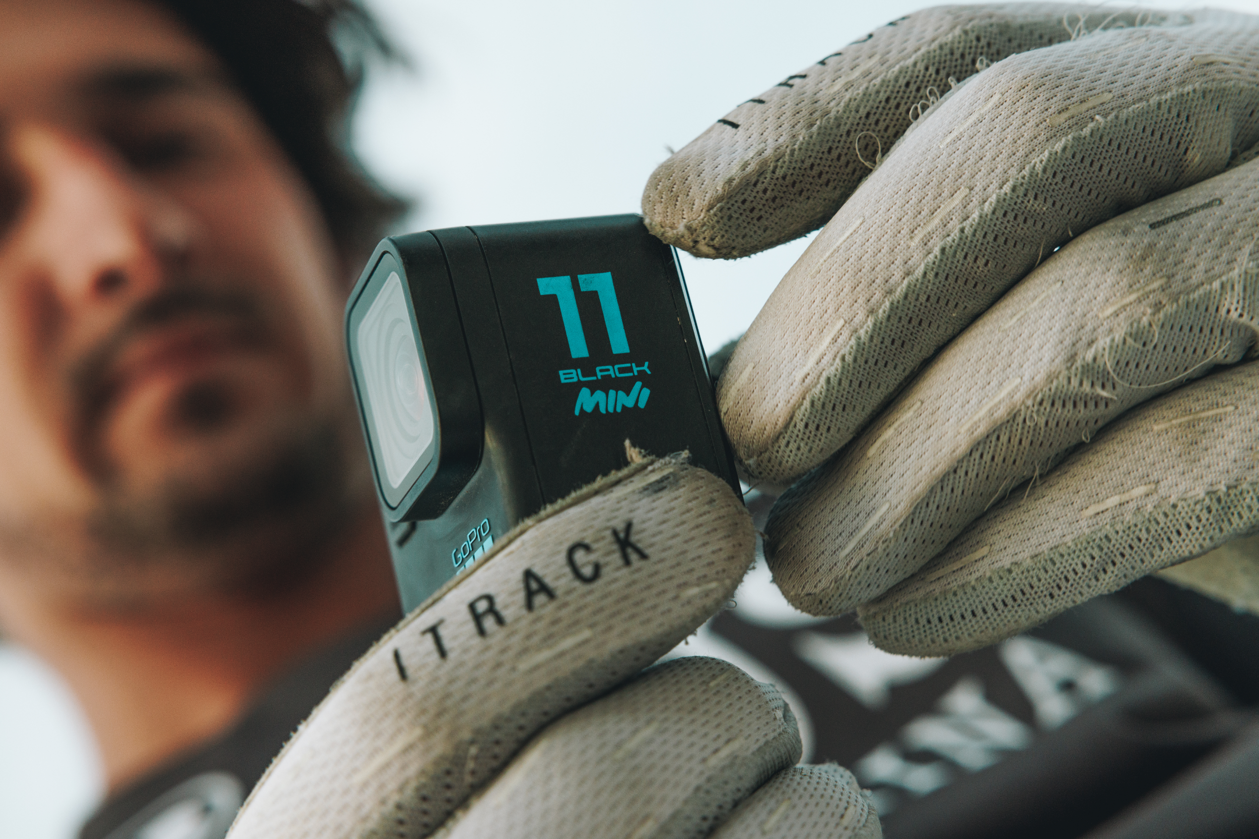 Eine Person hält eine schwarze GoPro-Kamera mit der Aufschrift '77 BLACK MINI'. Die Person trägt Handschuhe.