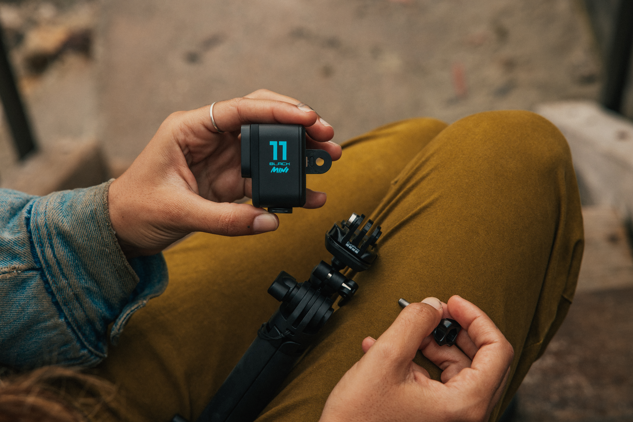 Hände halten eine schwarze GoPro-Kamera mit Mini-Bildschirm und Stativ.