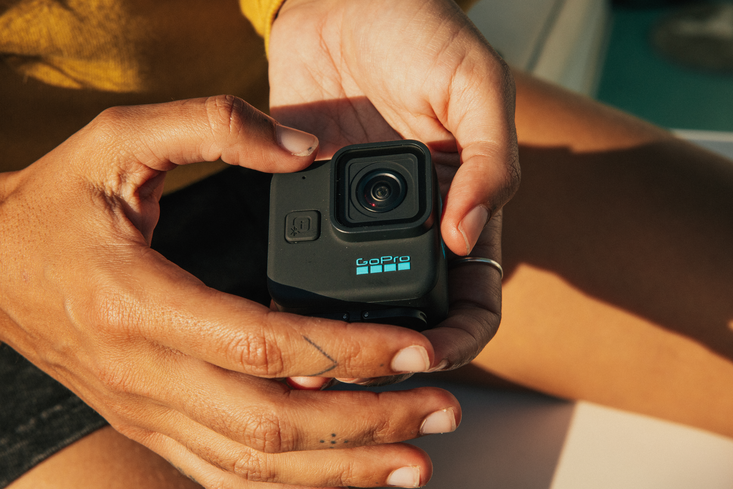 Hände einer Person, die eine kleine schwarze GoPro-Kamera halten, mit sichtbar GoPro-Logo.