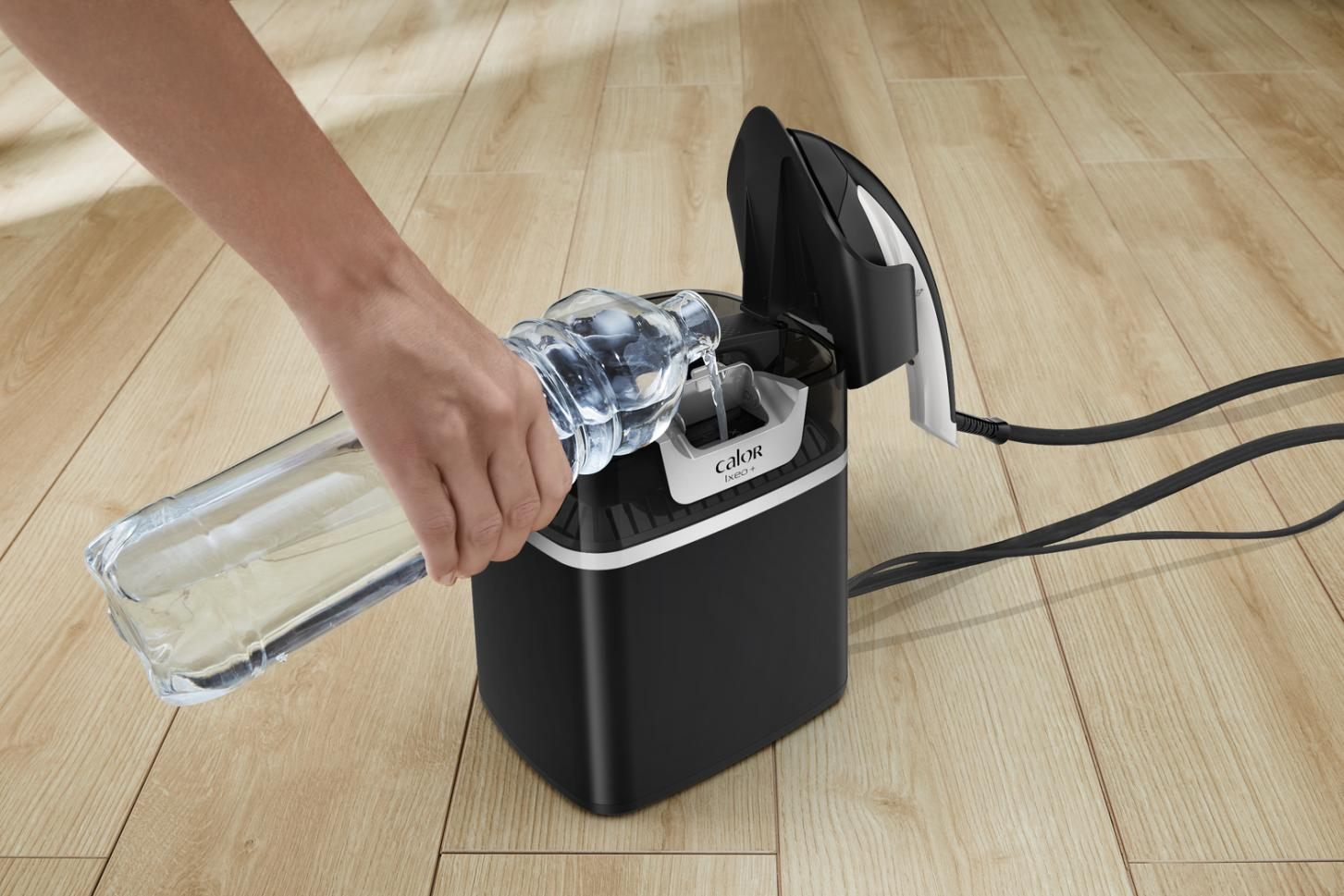 A person pouring water from a bottle into a black and white steam iron base.