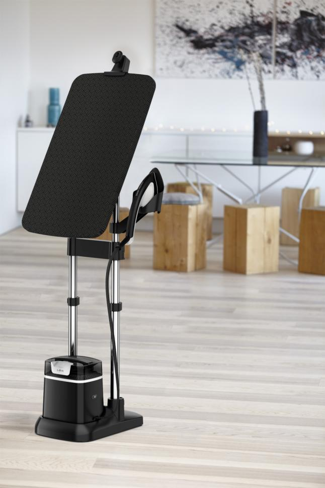 Black standing garment steamer with a black ironing board in a room setting.
