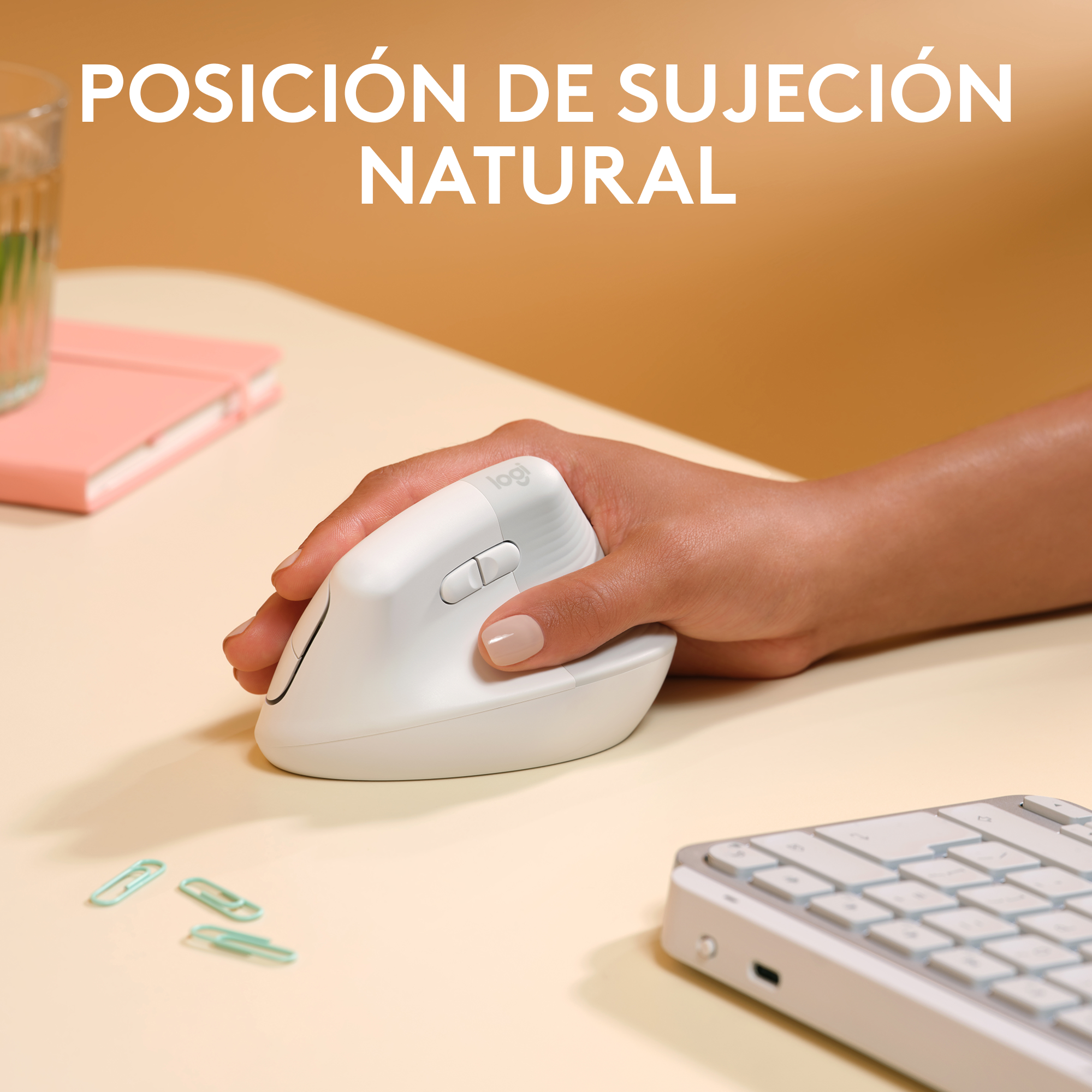 Una mano sostiene un ratón ergonómico Logitech blanco. Hay clips y un teclado en la escena.
