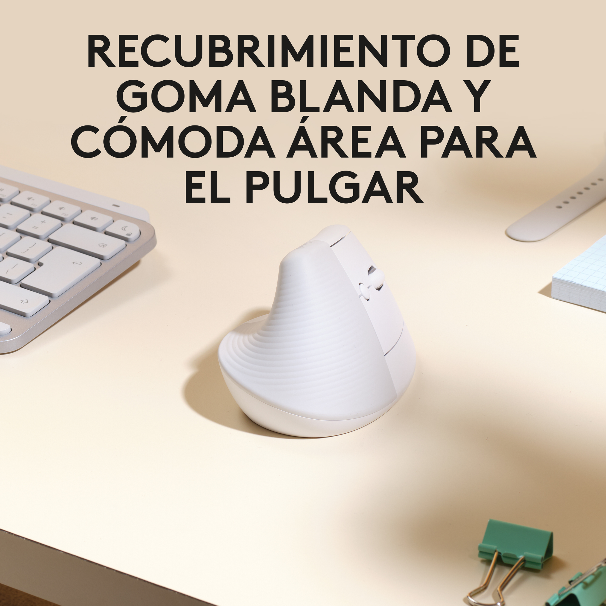 Ratón ergonómico blanco con texto en español, teclado y otros objetos de escritorio.