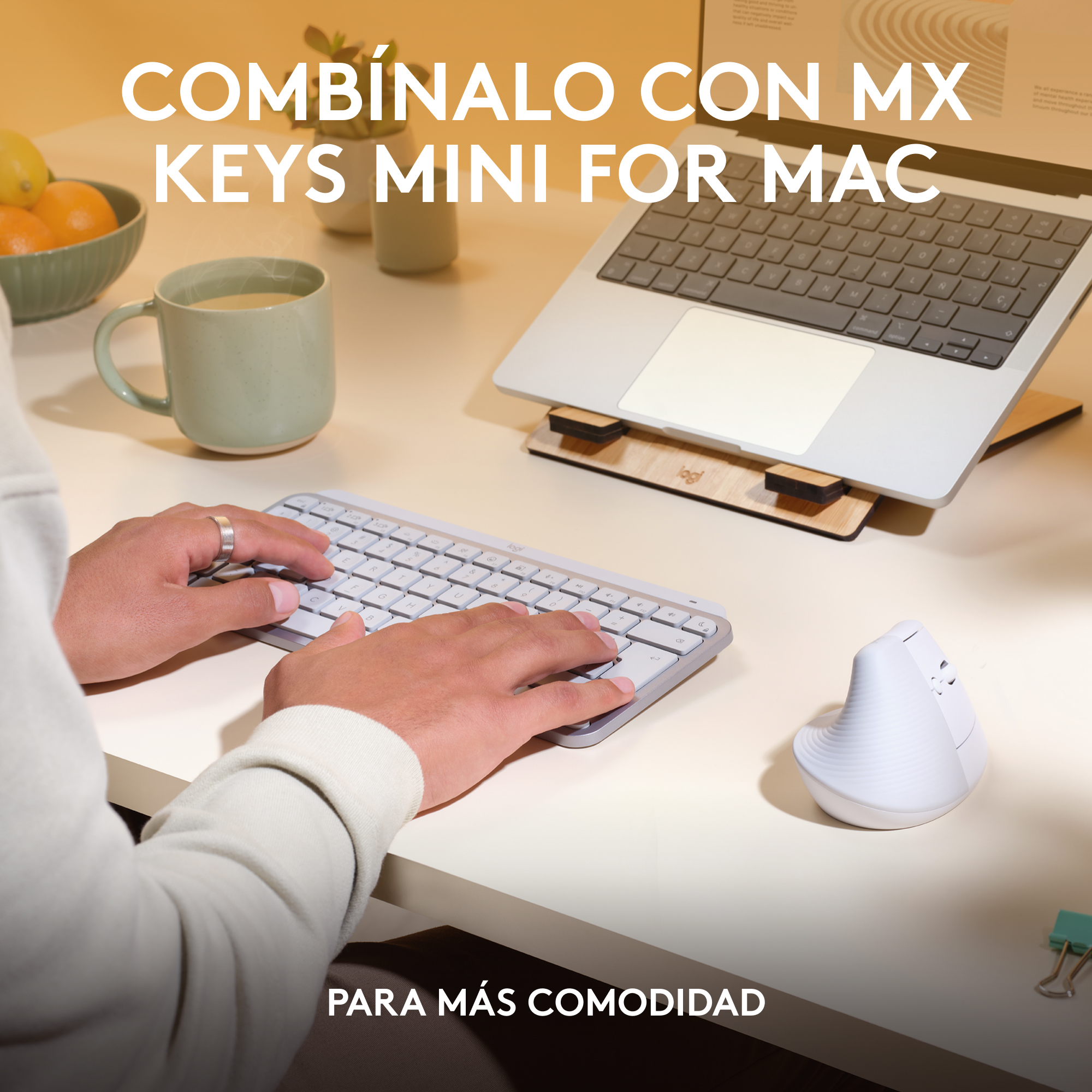 Una persona usando teclado y ratón. Hay un portátil en un soporte. El escritorio es blanco.