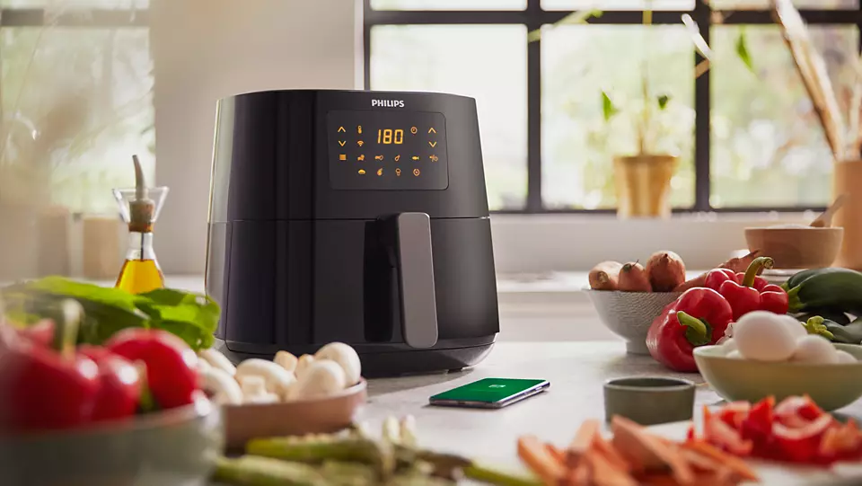 Black Philips air fryer on a table with vegetables and other cooking ingredients.
