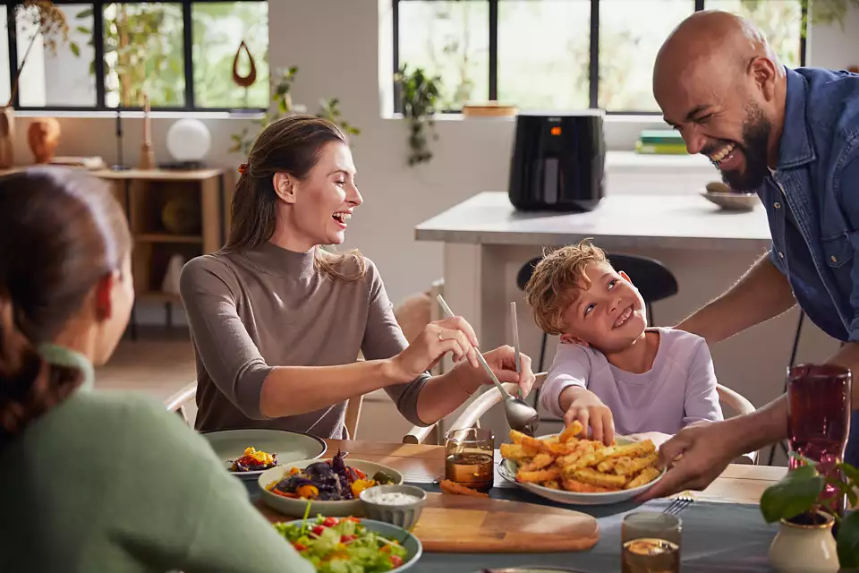 Family enjoying a meal with an air fryer on the table. People are smiling.