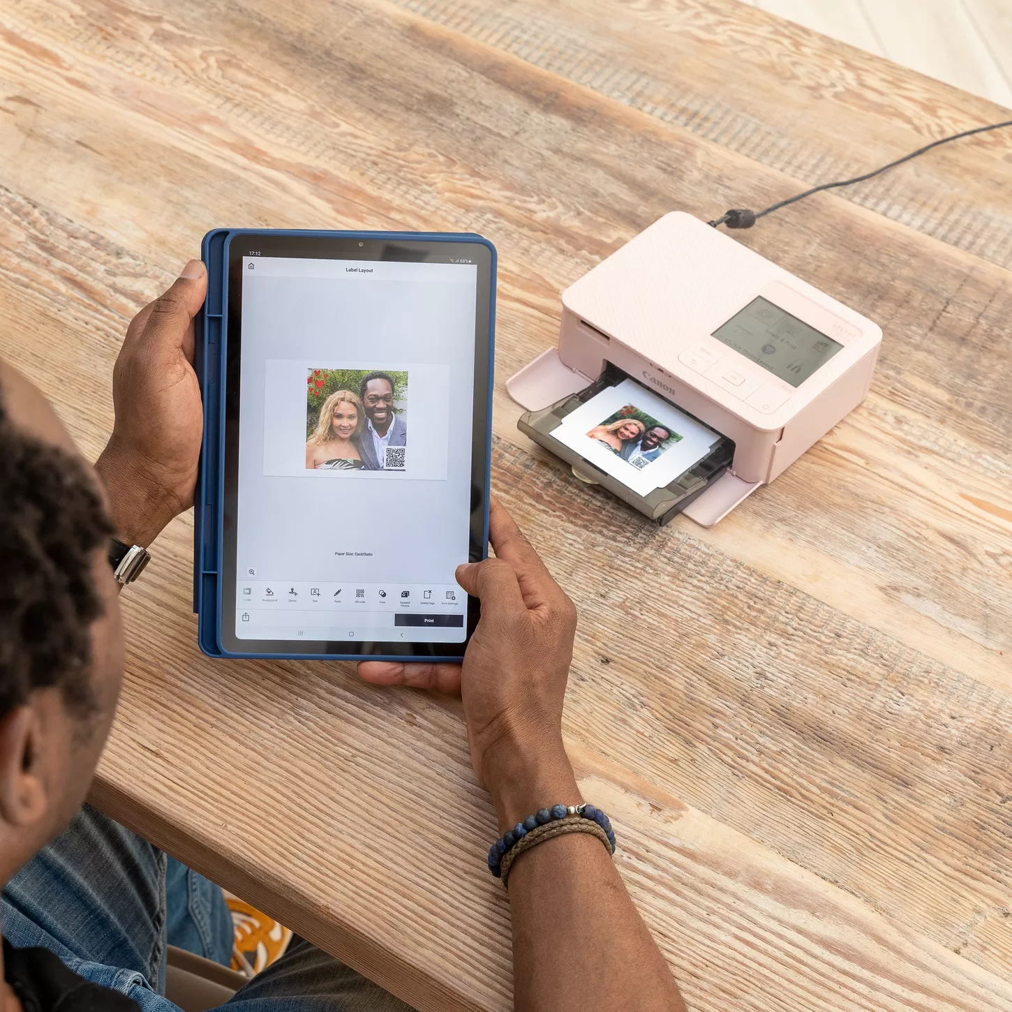 Una persona stampa foto da un tablet usando una stampante fotografica Canon rosa.