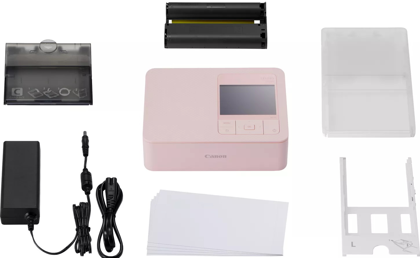 Stampante fotografica Canon Selphy rosa con accessori come inchiostro e carta. Tutto su sfondo bianco.