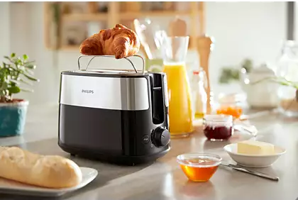 A toaster with a croissant on top, beside a bowl of honey and other breakfast items.