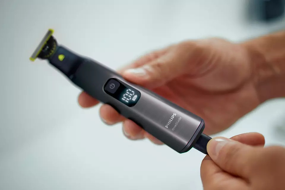 Handen houden een zwart Philips OneBlade elektrisch scheerapparaat vast. Het scherm toont de batterijduur.