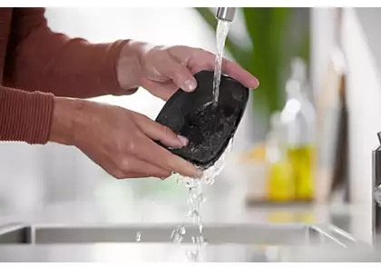 Mains lavant un appareil noir sous l'eau courante dans un évier, nettoyant un appareil.