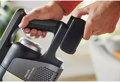 Handen die een batterij in een zwart-grijze stofzuiger plaatsen.