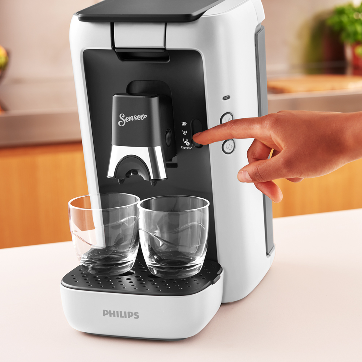 Wit-zwart Senseo koffiezetapparaat. Een hand drukt op de espressoknop. Twee glazen.
