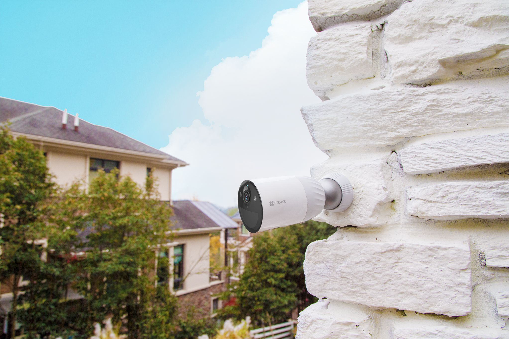 Une caméra de sécurité blanche montée sur un mur de briques blanches, avec un fond de ciel bleu.