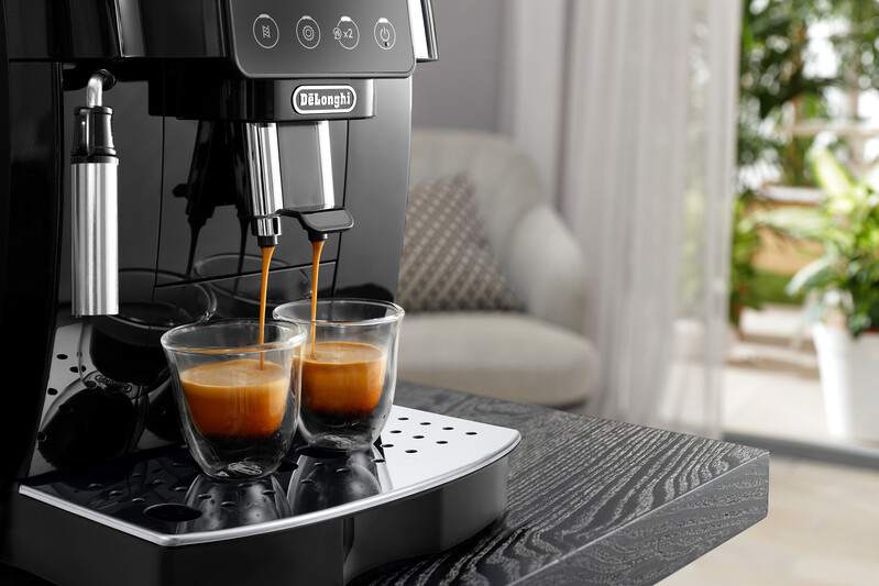 Black coffee machine brewing coffee into two glass cups on a dark wooden surface.