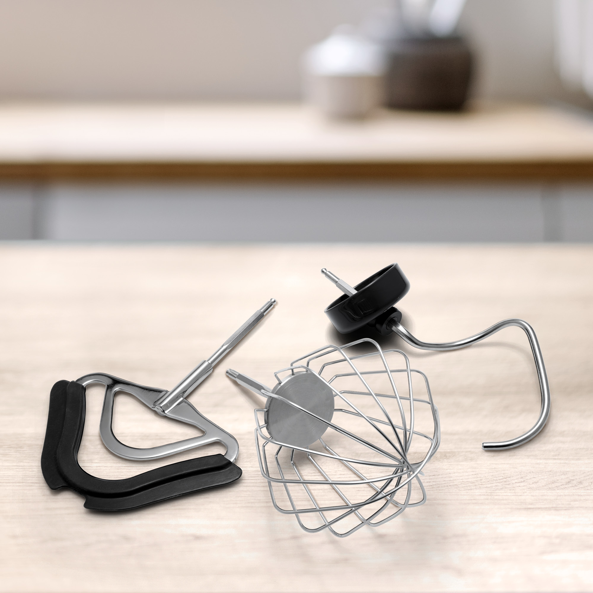 Gros plan sur les accessoires de mixeur sur une surface en bois : fouet, crochet pétrisseur et batteur.