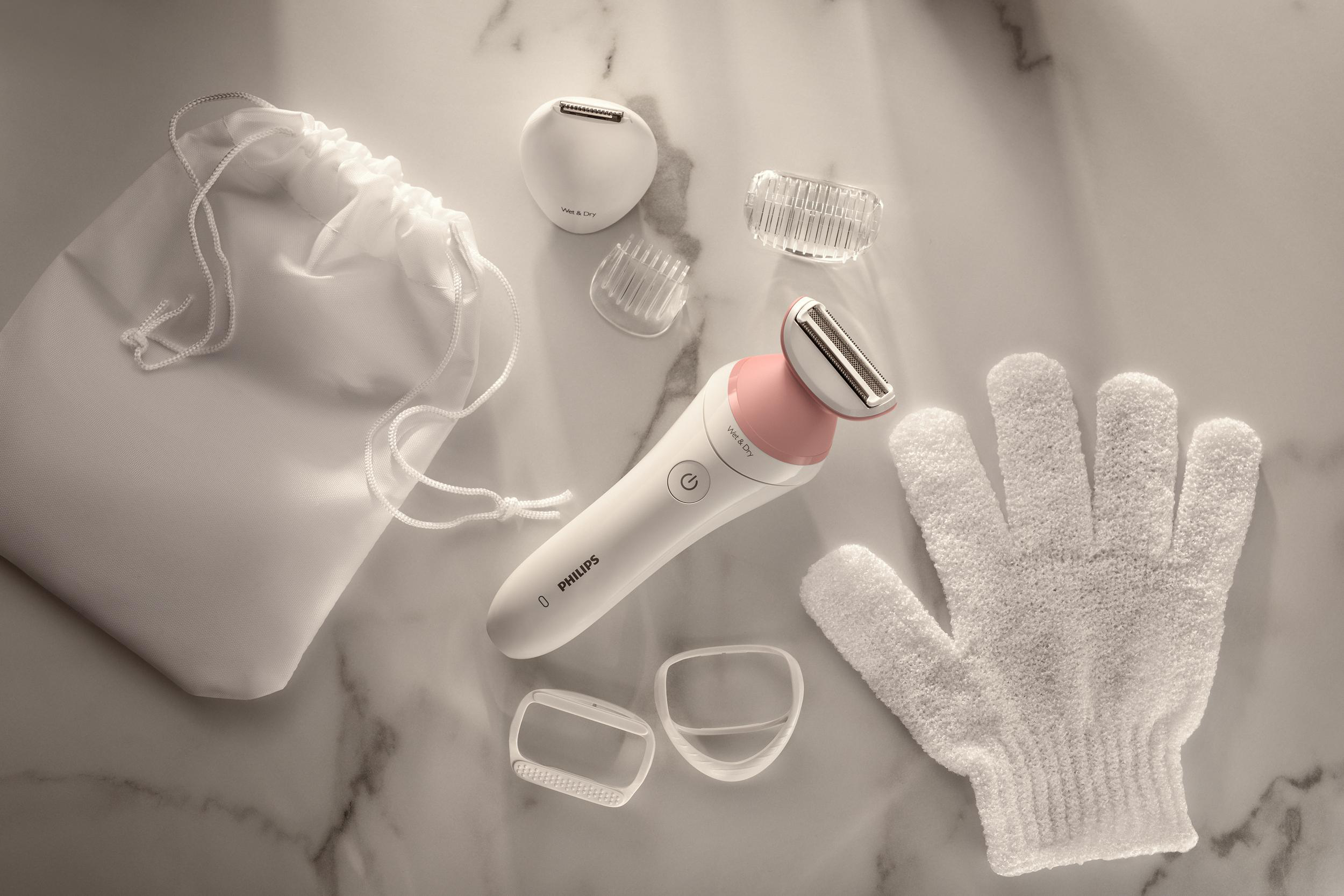 Ein weißes Philips-Gerät mit Zubehör: eine Tasche, Rasierköpfe und ein Handschuh auf Marmor.