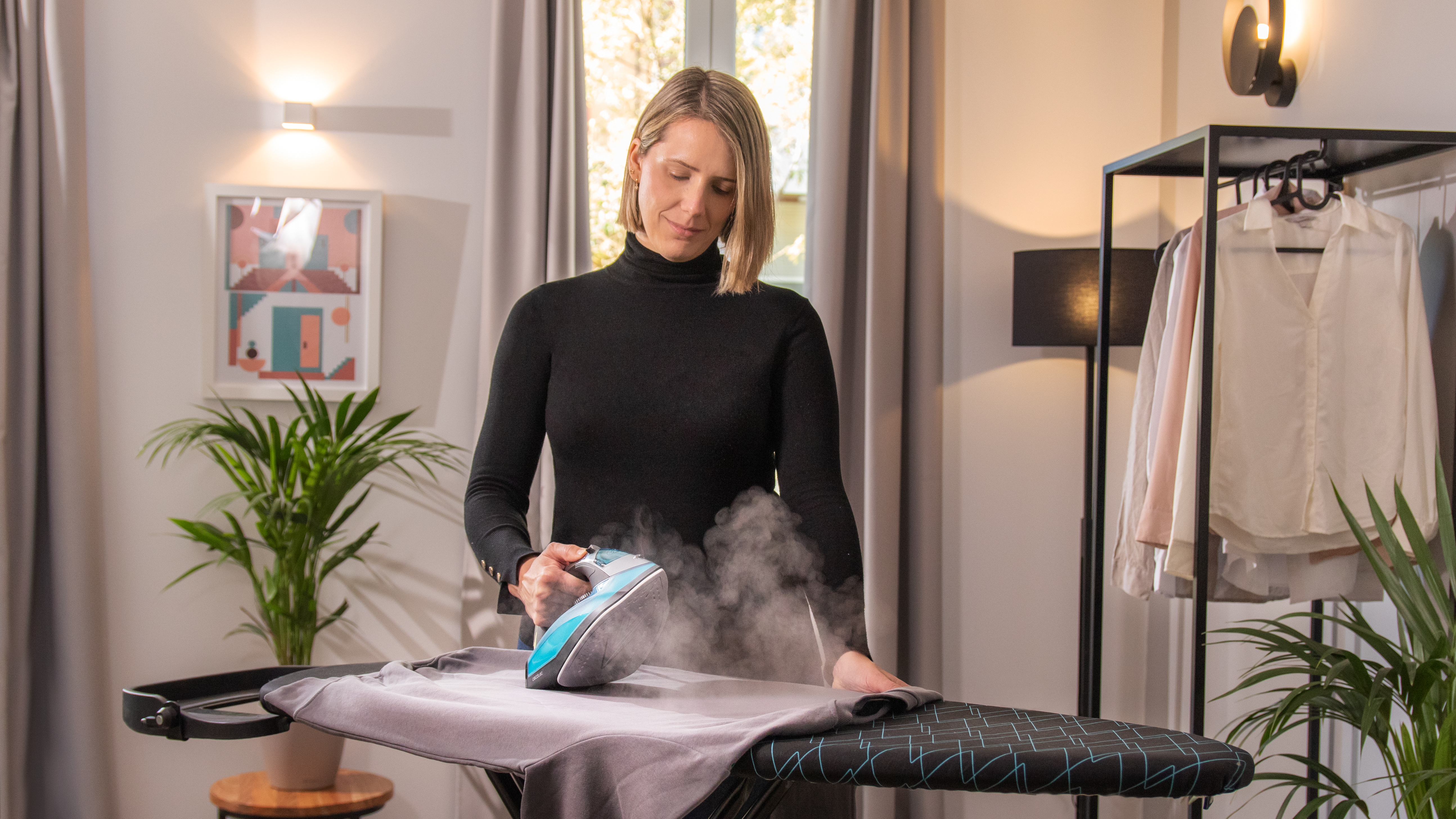 Mujer planchando una camisa gris en una tabla de planchar con vapor.