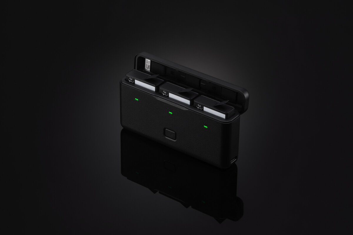 Eine schwarze Ladestation mit drei Steckplätzen und einem Deckel. Grüne Lichter zeigen den Ladestatus an. Dunkler Hintergrund.