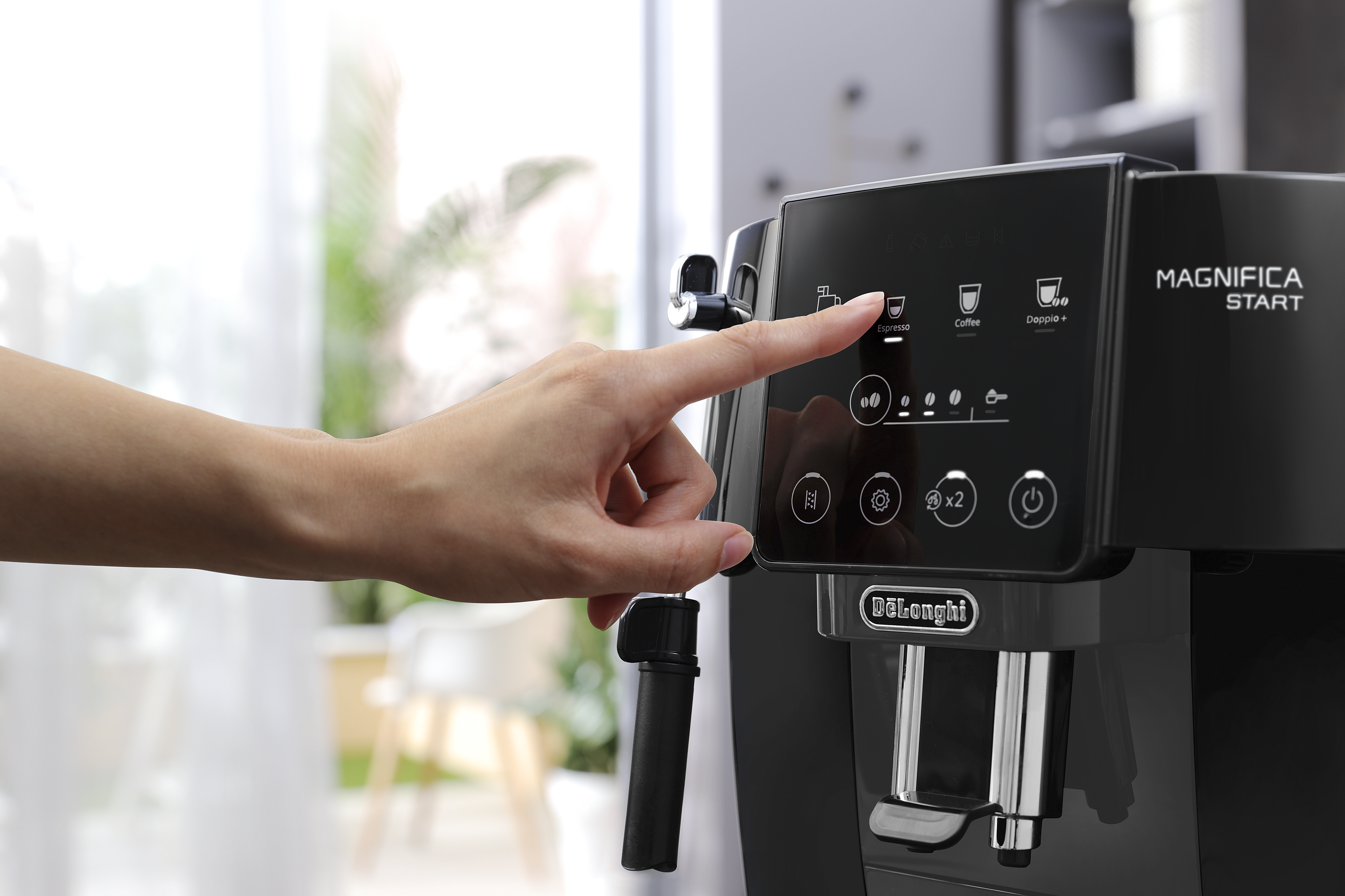 Une main touche l'écran d'une machine à café De'Longhi noire, avec d'autres boutons présents.