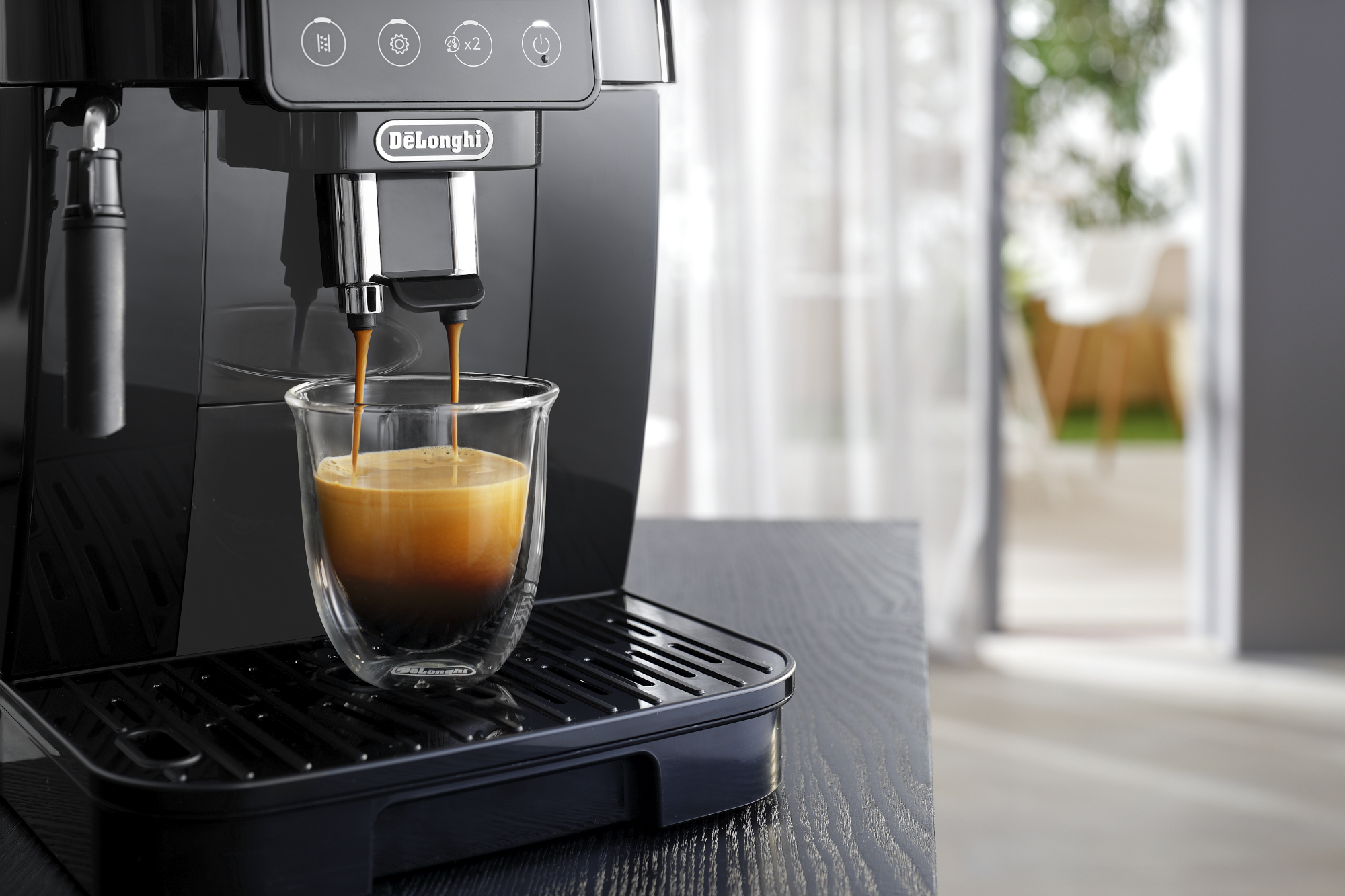 Une machine à expresso noire distribuant du café dans une tasse en verre transparent sur un plateau noir.