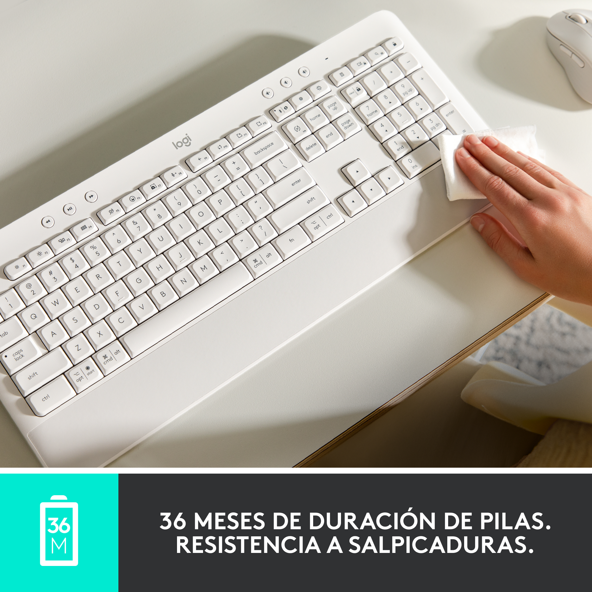 Persona limpiando un teclado blanco con un paño blanco sobre una superficie blanca.