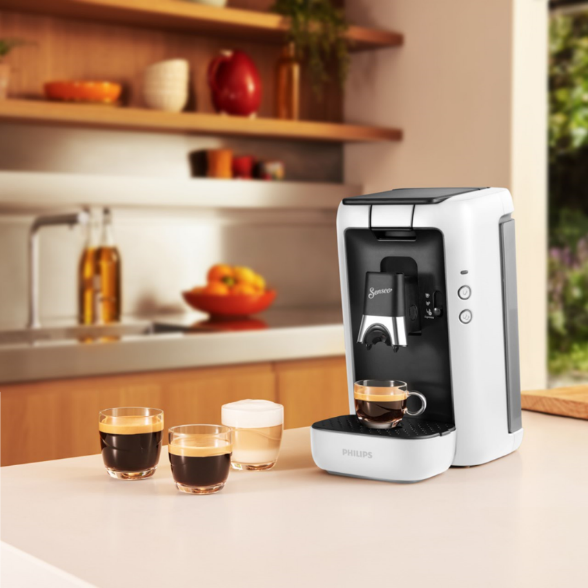 Wit-zwarte koffiemachine met een kopje koffie, naast glazen.