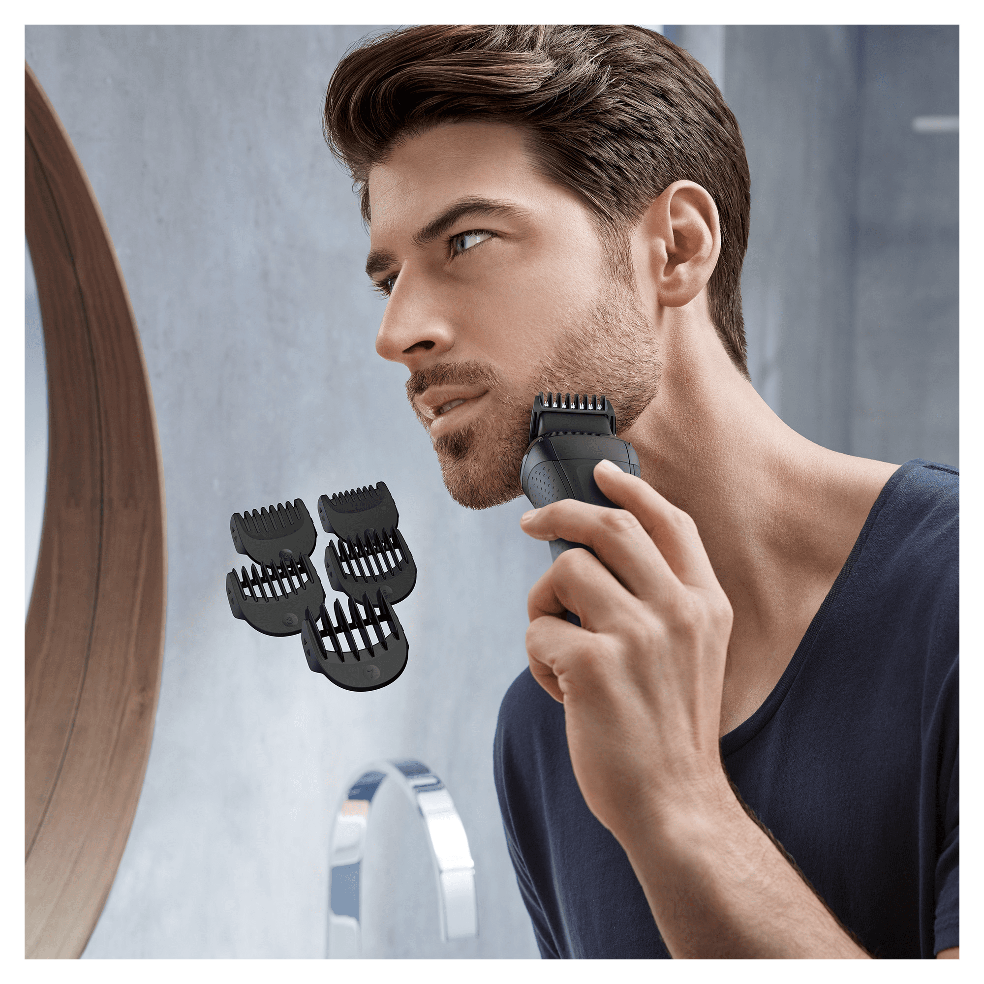 Man using a beard trimmer with several black comb attachments visible on the counter.
