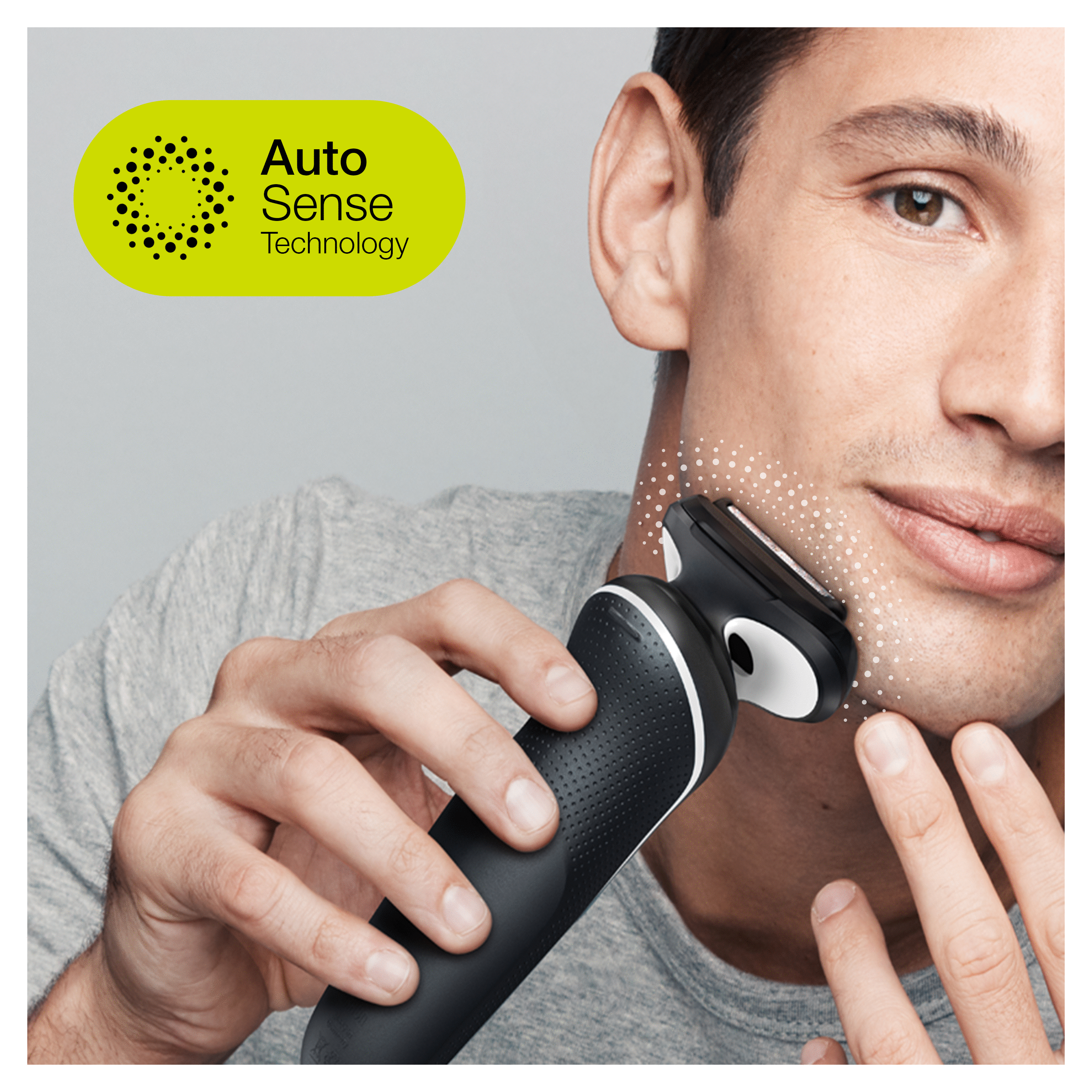 A man shaves his face with a black and white electric shaver, with a green Auto Sense logo in view.