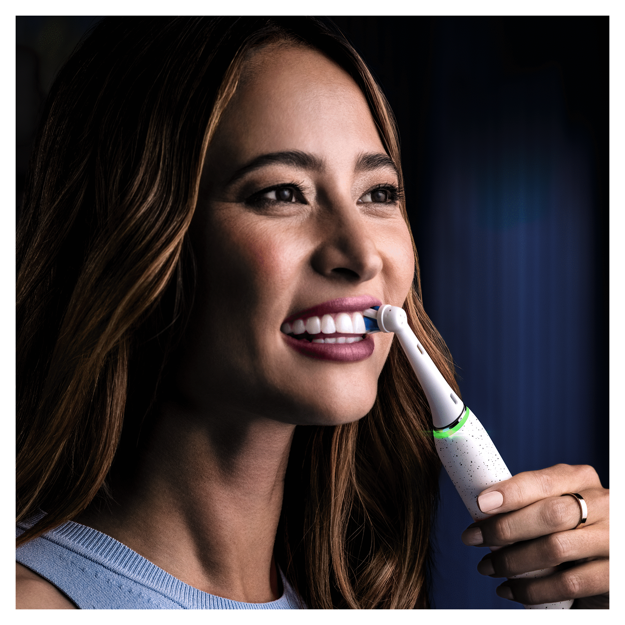 A woman brushing her teeth with an electric toothbrush, smiling. White and blue tones.
