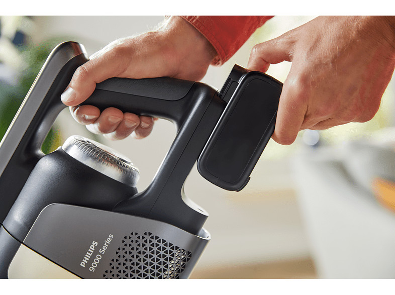 Handen die de handgreep van een stofzuiger vasthouden, een batterij plaatsen.