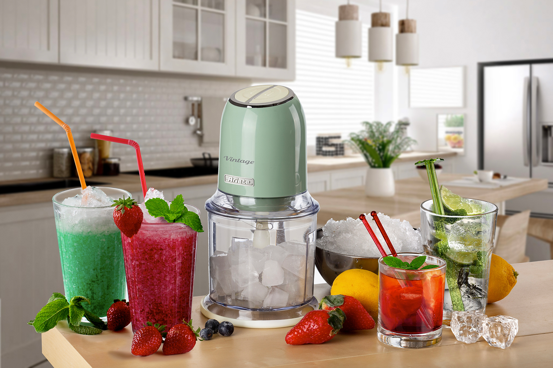 Ein grün-weißer Blender im Vintage-Stil mit Getränken und Eis in Gläsern sowie Obst auf einem Holztisch.