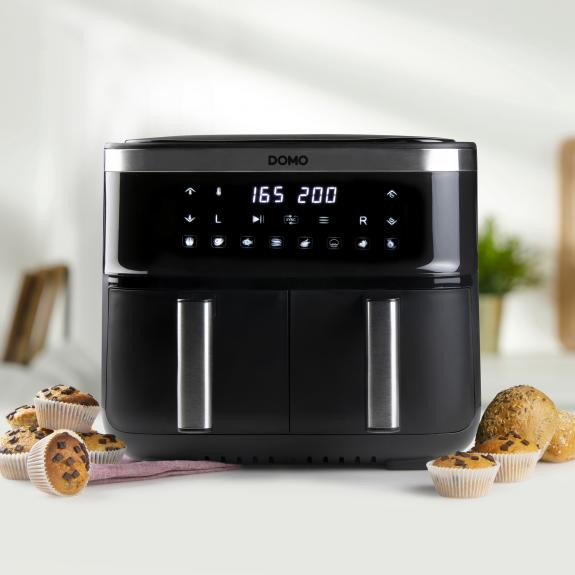 Black air fryer with digital display, surrounded by muffins and bread rolls on a table.