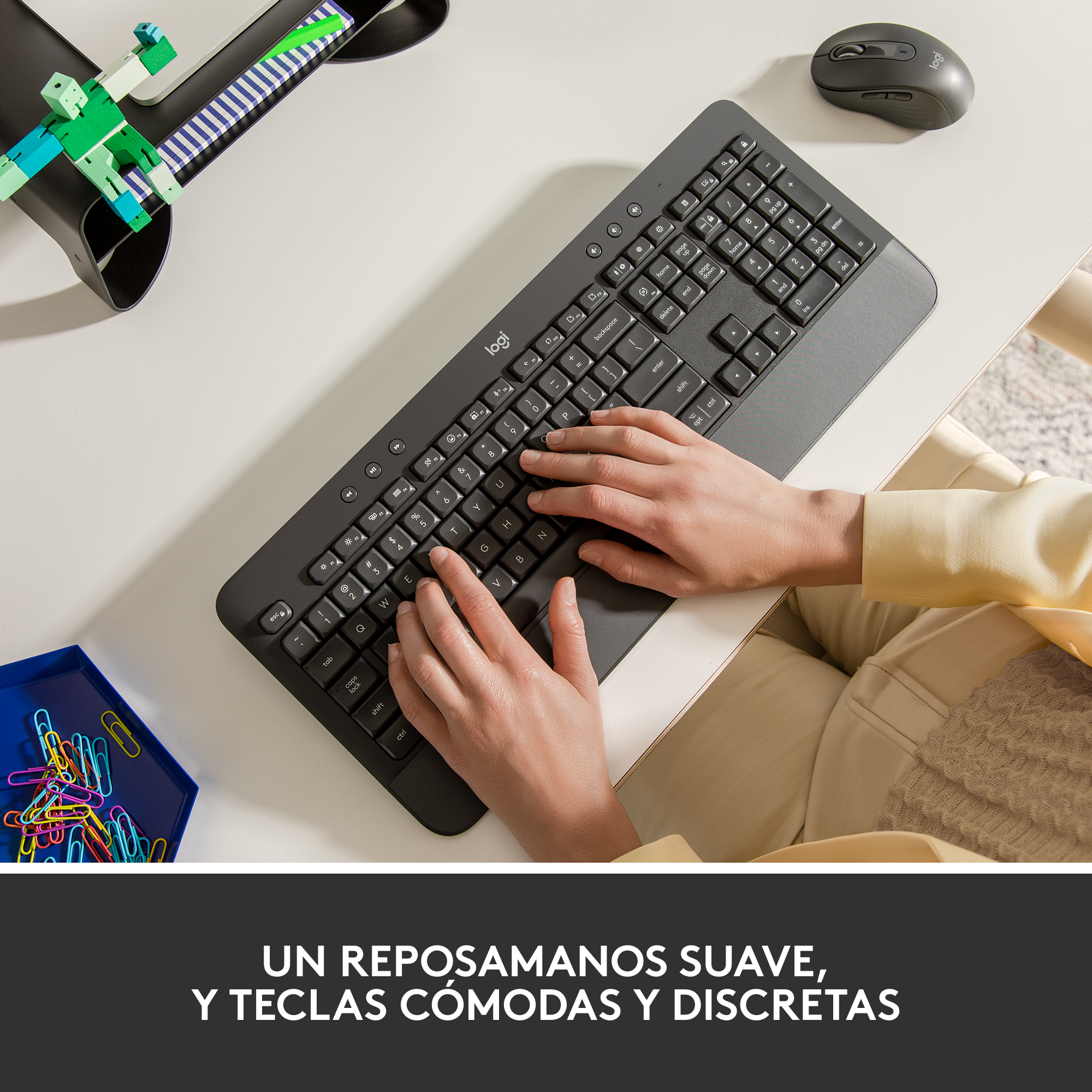 Manos en un teclado, con un ratón y una bandeja azul con clips de colores.
