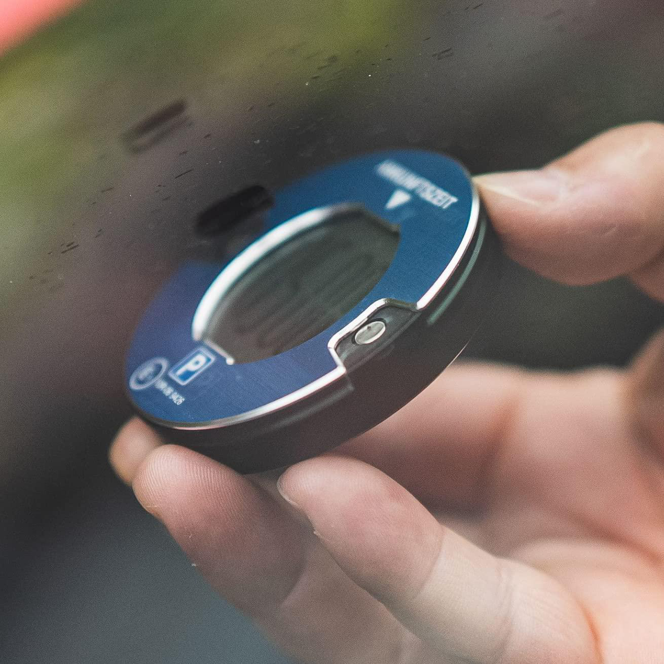 Eine Hand, die eine blau-silberne Parkscheibe hält. Sie hat eine Digitalanzeige und ein Parksymbol.