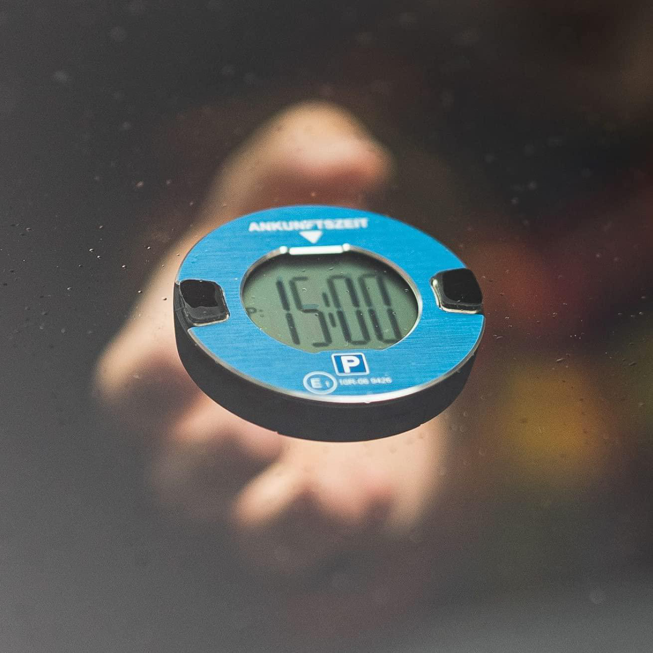 Blaue Parkscheibe an einem Autofenster. Zeigt die Zeit 15:00 Uhr. Hand im Hintergrund.