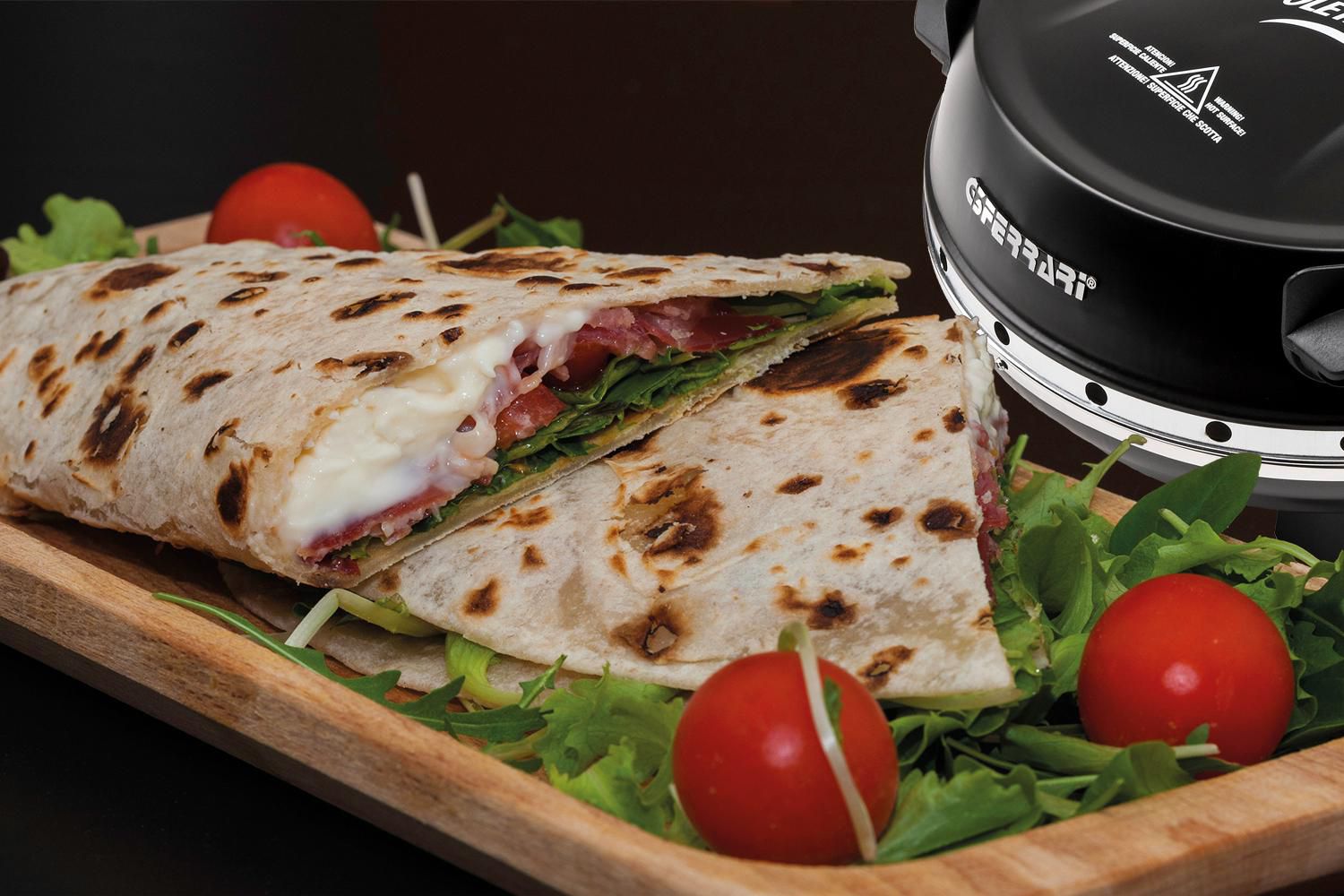 Ein Piadina-Sandwich, halbiert, mit Käse, Fleisch und Gemüse, auf einem Holztablett, mit Tomaten.