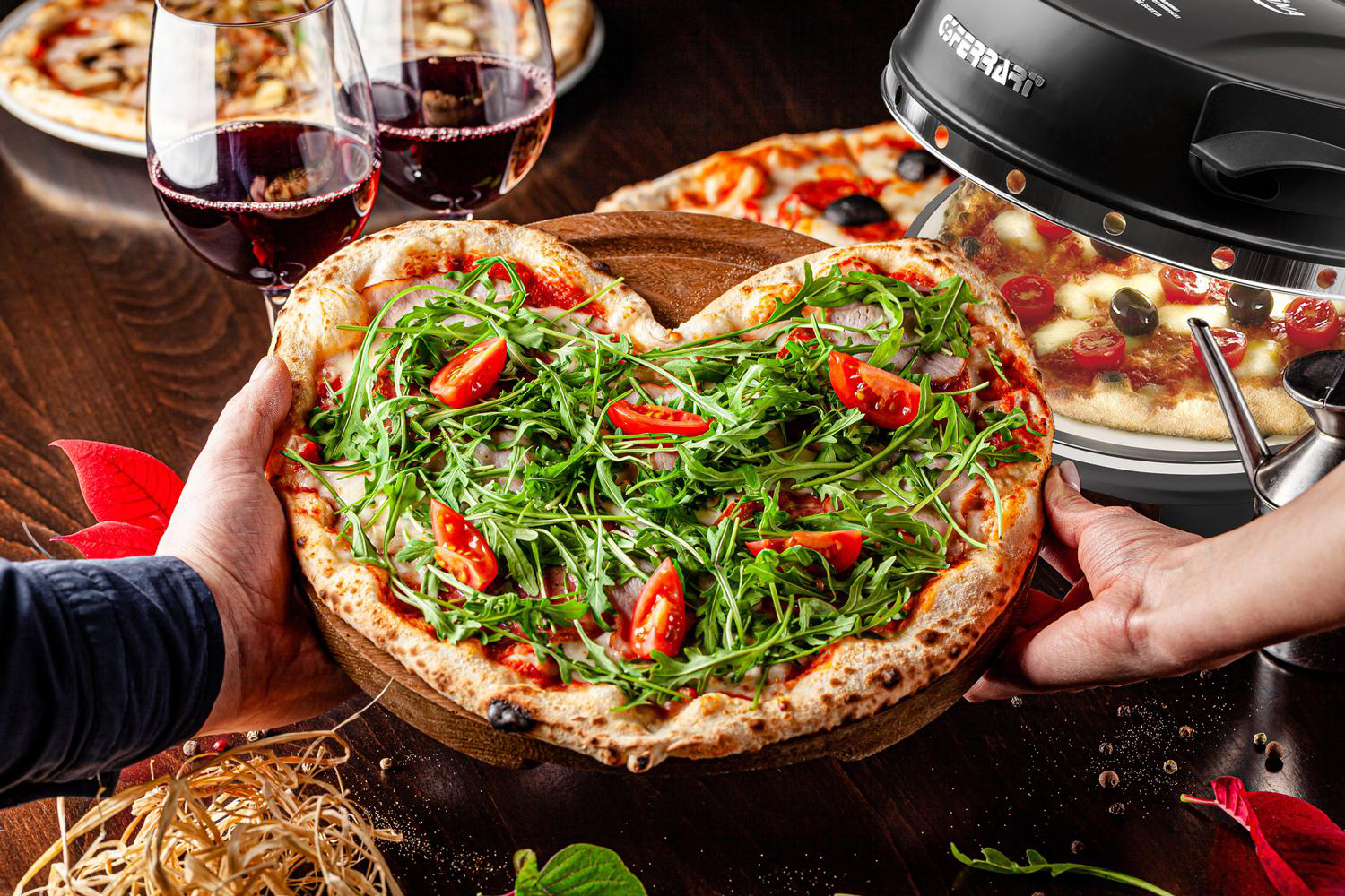 Herzförmige Pizza, die von Händen gehalten wird. Zwei Weingläser und eine weitere Pizza auf dem Holztisch.