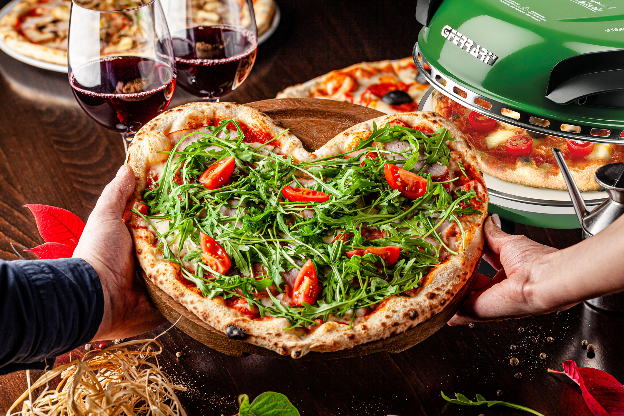 Eine herzförmige Pizza mit Rucola und Tomaten, gehalten von zwei Personen, Weingläser.
