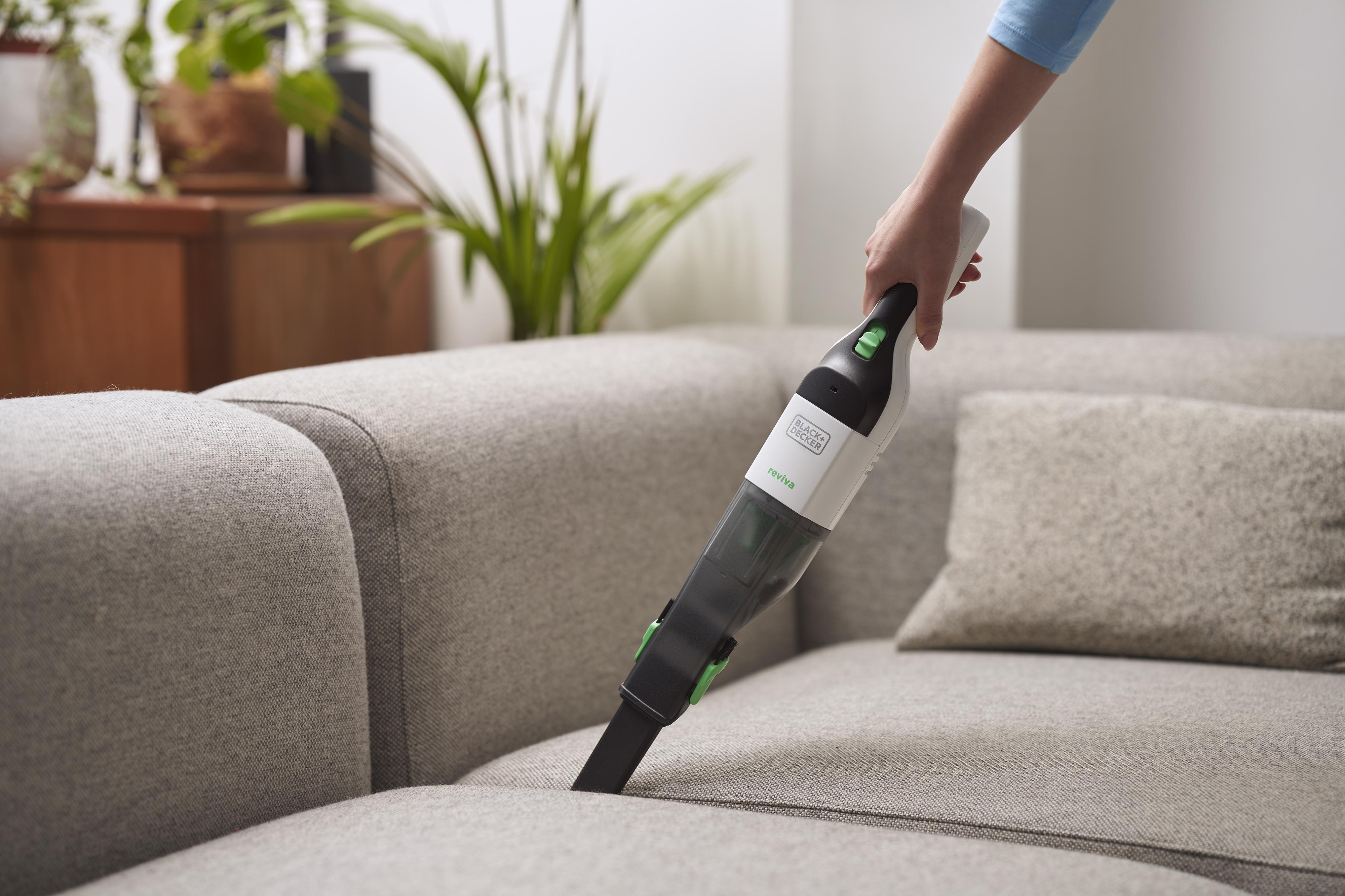 Person benutzt einen Handstaubsauger auf einer grauen Couch.