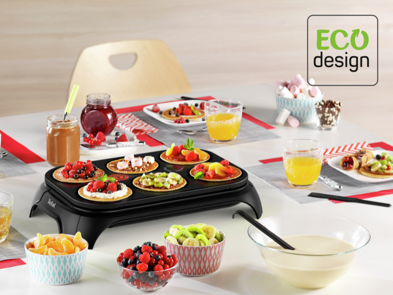 Crêpes sur une plaque noire, garnies de fruits. Bols de fruits et de jus sur une table blanche.