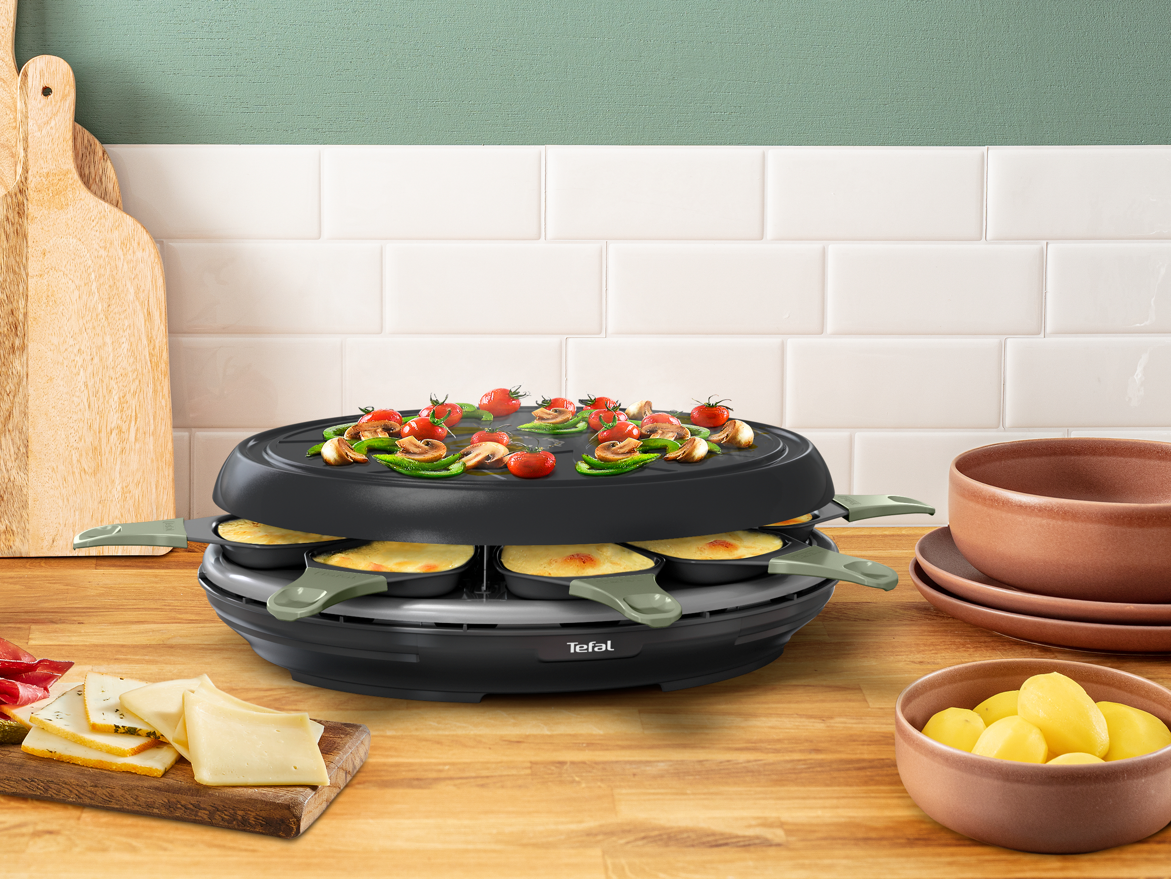 A raclette grill with cheese and vegetables, and plates on the side.