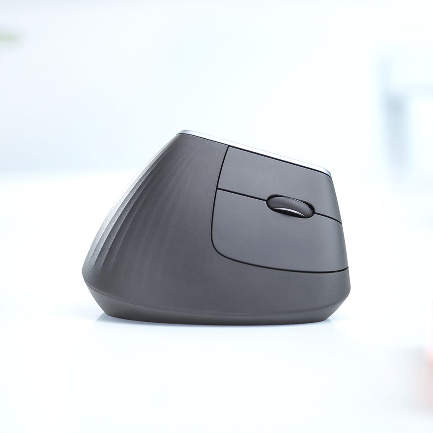 Un ratón ergonómico gris oscuro. Tiene una rueda de desplazamiento y está sobre una superficie blanca.