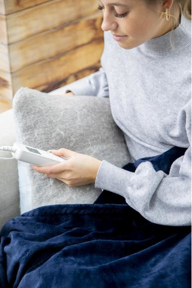 Woman holding a white controller on a navy blue blanket. She's sitting on a gray cushion.