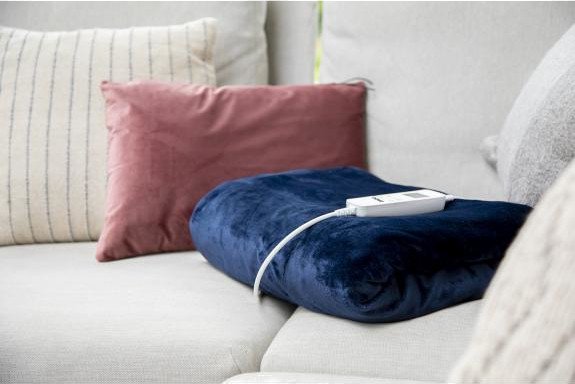 Blue heated blanket on a couch. There are pillows in the background.
